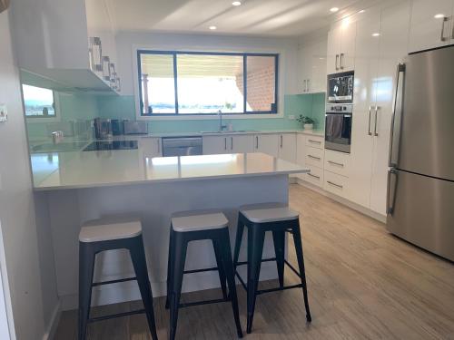a kitchen with two bar stools and a counter with a refrigerator at Ranges Over the Bay in Culburra Beach