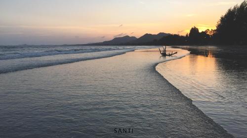 a beach at sunset with a boat in the water at SANTI beach retreat in Ban Rang Pla