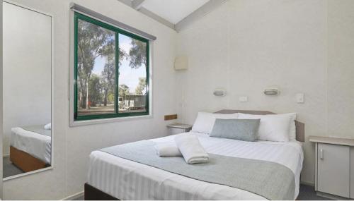 a white bedroom with a large bed and a window at Apex RiverBeach Holiday Park in Mildura