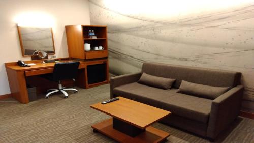 a living room with a couch and a desk and a mirror at Odysis Suites Osaka Airport Hotel in Izumi-Sano