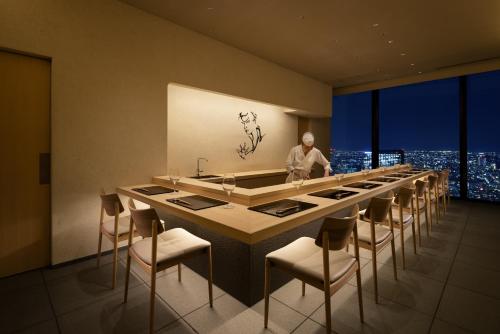 a man standing in a room with a long bar with chairs at BELLUSTAR TOKYO, A Pan Pacific Hotel in Tokyo