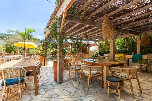 a patio with tables and chairs under a wooden pergola at Hôtel La Piscine in Le Lavandou