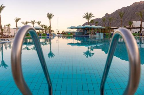 a swimming pool with palm trees and mountains in the background at Happy Life Village Dahab in Dahab