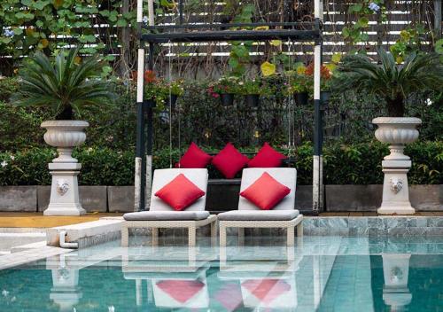 two chairs with red pillows sitting next to a pool at Le Thatluang D'oR Boutique Hotel in Vientiane