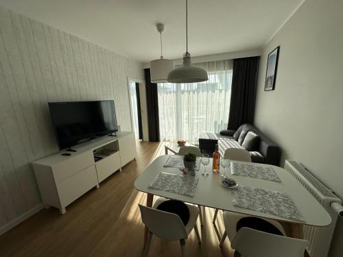 uma sala de estar com uma mesa com cadeiras e uma televisão em Gąski Apartament Nadmorski em Gąski