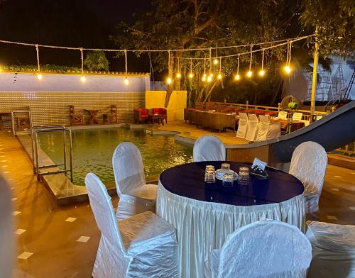 einen Tisch mit Stühlen und einen Pool in der Nacht in der Unterkunft Monalisa lawns in Thane