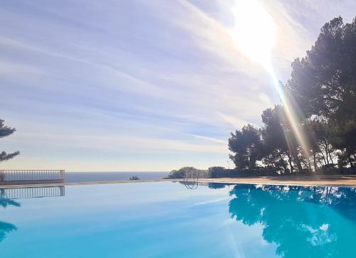 una piscina de agua con el sol en el cielo en SUPERBE STUDIO VUE MER - Plage, Piscine ET Tennis Prive, en Bandol