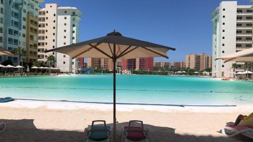 a umbrella sitting on the beach next to a pool at Two Bedrooms for Families only Chalet Sia Lagoon Golf Porto Marina للعائلات فقط شاليه غرفتين كريستال لاجون جولف بورتو مارينا in El Alamein