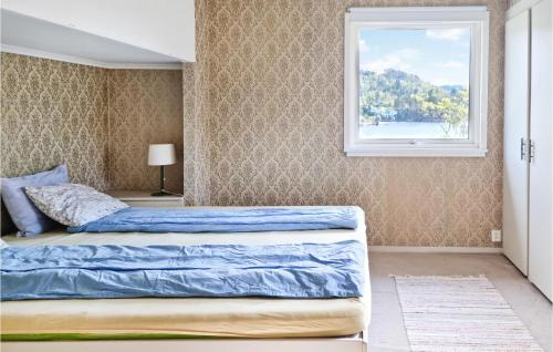 Schlafzimmer mit einem Bett mit blauer Bettwäsche und einem Fenster in der Unterkunft Nice Home In Lyngdal With House Sea View in Lyngdal