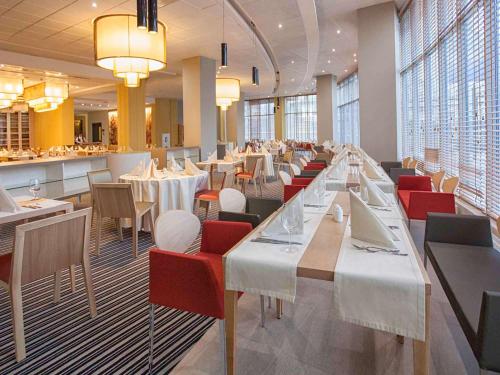 un restaurante con mesas blancas y sillas rojas en Mercure Lipetsk Center, en Lipetsk