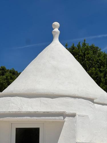 a white building with a funnel top with trees in the background at Trullo Moi in Ostuni