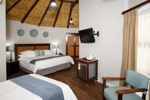 a bedroom with two beds and a tv and a chair at Protea Hotel by Marriott Oudtshoorn Riempie Estate in Oudtshoorn