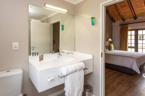 a bathroom with a sink and a toilet and a bed at Protea Hotel by Marriott Oudtshoorn Riempie Estate in Oudtshoorn