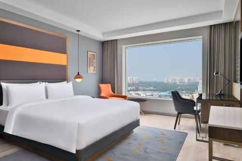 a bedroom with a bed and a desk and a large window at Le Meridien Hyderabad in Hyderabad