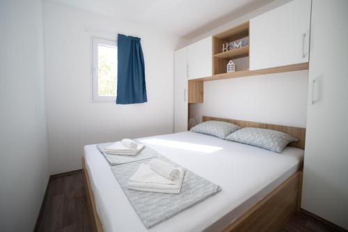 a small bedroom with a white bed with a window at Mobile Home Lana in Murter