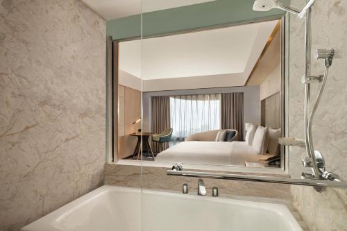 a bathroom with a bath tub and a bedroom at Sari Pacific Jakarta, Autograph Collection in Jakarta