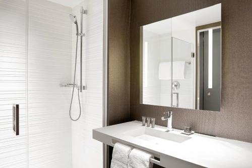 a bathroom with a sink and a mirror and a shower at AC Hotel by Marriott Irvine in Irvine
