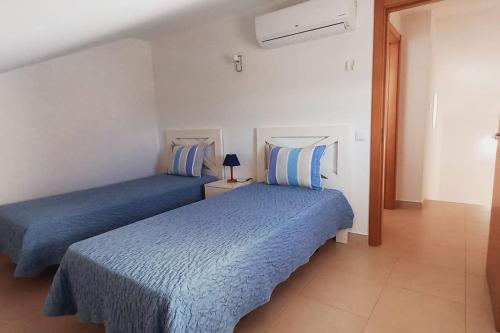 Duas camas num quarto branco com lençóis azuis em Apartamento Sol e Mar em Vila Nova de Cacela