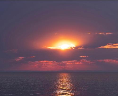 a sunset over the ocean with the sun in the clouds at Gite de la Baie Hatée in Bic