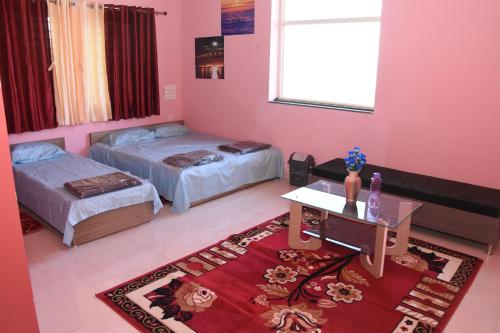 a bedroom with two beds and a table and a rug at H P HomeStay in Dhārwād