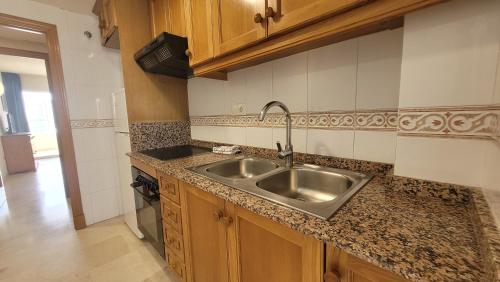 una cocina con fregadero de acero inoxidable y armarios de madera en Gemelos 22-Fincas Benidorm, en Benidorm