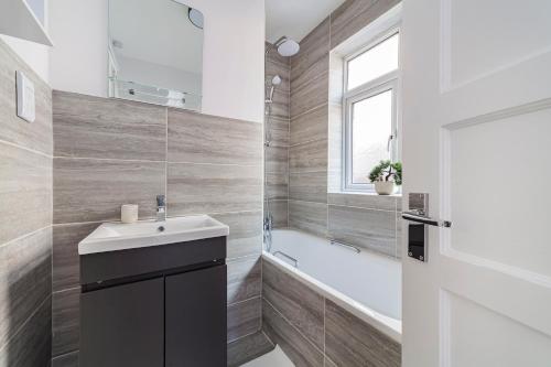 a bathroom with a sink and a tub and a window at The Neasden Villas in London