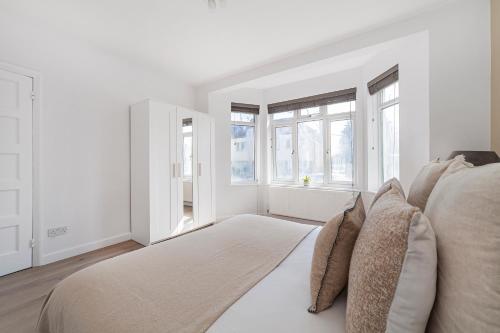 a white bedroom with a large bed with windows at The Neasden Villas in London