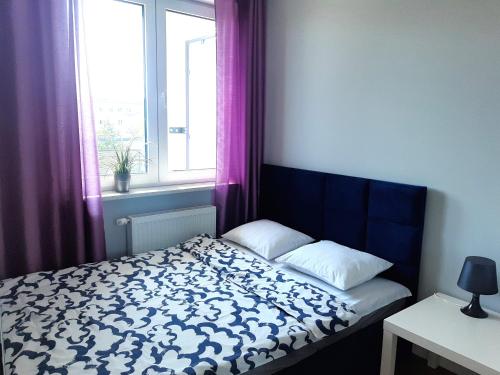 een slaapkamer met een bed en een raam met paarse gordijnen bij Apartament Wawa in Warschau