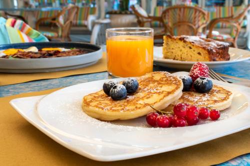 a plate of pancakes with fruit and a glass of orange juice at Hotel Ettoral in Lido di Jesolo