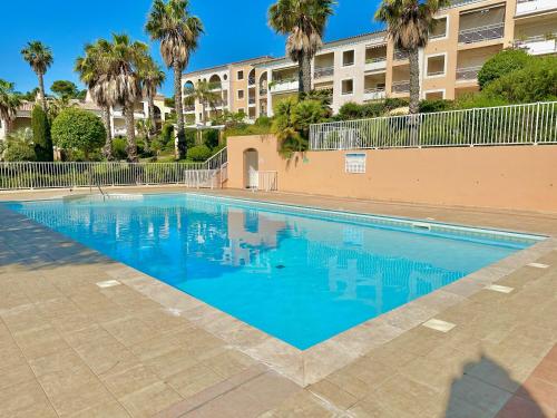 une piscine avec des palmiers et un bâtiment dans l'établissement T2 avec jardin, clim & piscine - Proche plages et randos, parking privé - La Rascasse, à Hyères