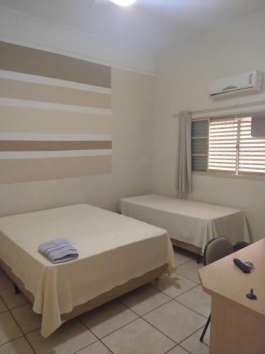 a room with two beds and a desk and a window at Hotel Dublin in Araraquara