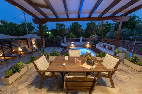 a patio with a wooden table and chairs and a pool at Villa Filyra in Kato Gatzea