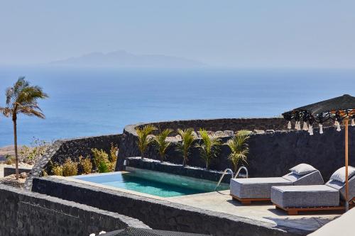 a swimming pool with chairs and an umbrella and the ocean at Theano Cave Suites & Villas in Imerovigli
