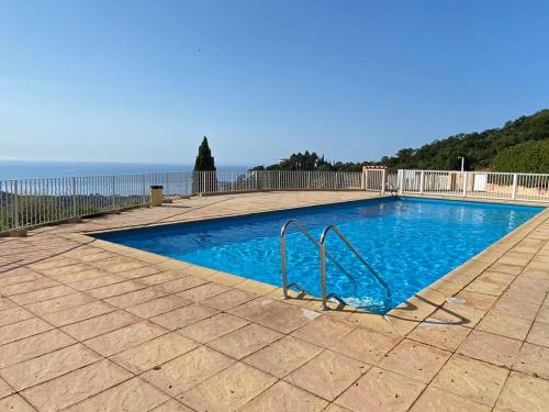 una piscina azul con una valla y el océano en Location vacance vue mer 4 à 6 personnes, en Cavalaire-sur-Mer