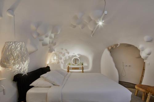 a white bedroom with a bed and a table at Theano Cave Suites & Villas in Imerovigli