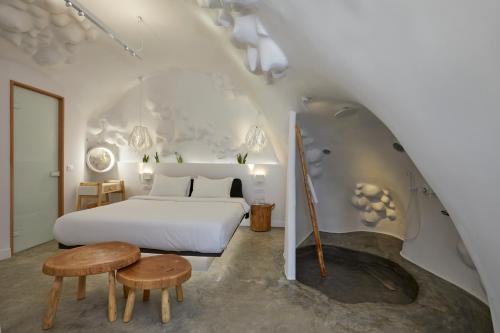 Schlafzimmer mit einem weißen Bett und Holztischen in der Unterkunft Theano Cave Suites & Villas in Imerovigli