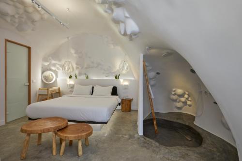 sypialnia z białym łóżkiem i drewnianymi stołami w obiekcie Theano Cave Suites & Villas w Imerovíglion