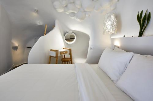 a white bedroom with two beds and a table at Theano Cave Suites & Villas in Imerovigli