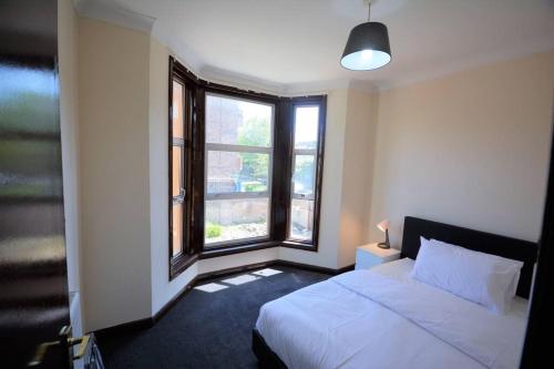 sypialnia z białym łóżkiem i 2 oknami w obiekcie Lovely 3bedroom Apartment London w Londynie