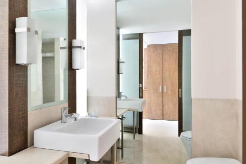 Four Points by Sheraton Bengaluru Whitefield في بانغالور: حمام مع حوض أبيض ومرآة
