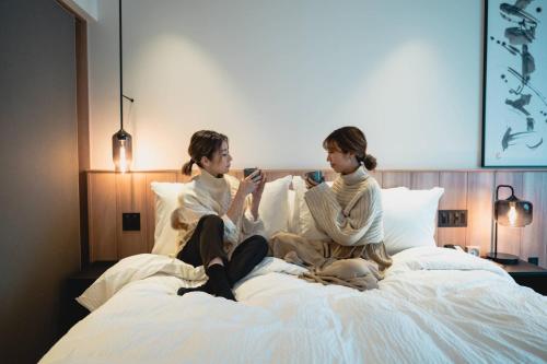 two girls sitting on a bed drinking coffee at Fairfield by Marriott Gifu Gujo in Gujo