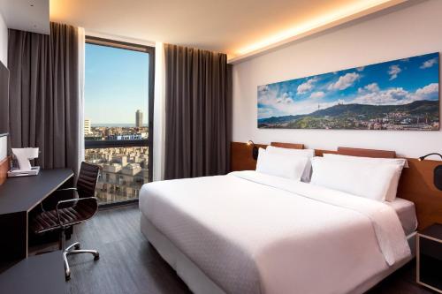 バルセロナにあるフォーポイント バイ シェラトン バルセロナ ディアゴナルのベッド、デスク、窓が備わるホテルルームです。