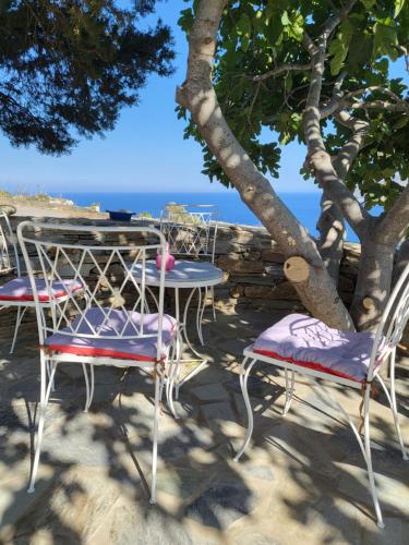 a table and chairs under a tree on the beach at Houlia home διαμέρισμα με δωρεάν χώρο στάθμευσης in Andros