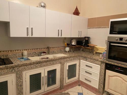 une cuisine avec des armoires blanches et un micro-ondes dans l'établissement Appartement Yasin Meknes, à Meknès