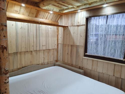 a bed in a wooden room with a window at Planinska Bajka pogodna za dnevne boravka i one koji se vole in Olovo