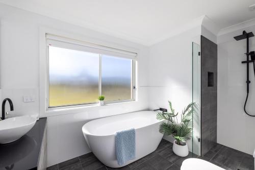 baño blanco con bañera y ventana en Whale Studio Suite, en Anna Bay