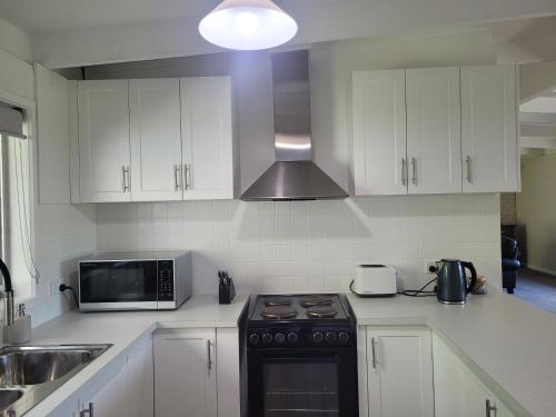 a kitchen with white cabinets and a stove and a microwave at Healesville Schofield Cottage in Healesville