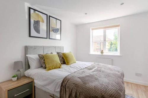a bedroom with a bed with yellow pillows and a window at Lovegrove House - Modern 3 bed house for business or family stay with free parking in Slough