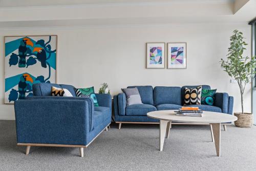 メルボルンにあるNook Melbourne Apartmentsのリビングルーム(青いソファ2台、テーブル付)
