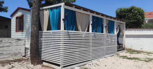 a white shed with blue curtains and a tree at Mobile Homes Inalex Relax in Privlaka